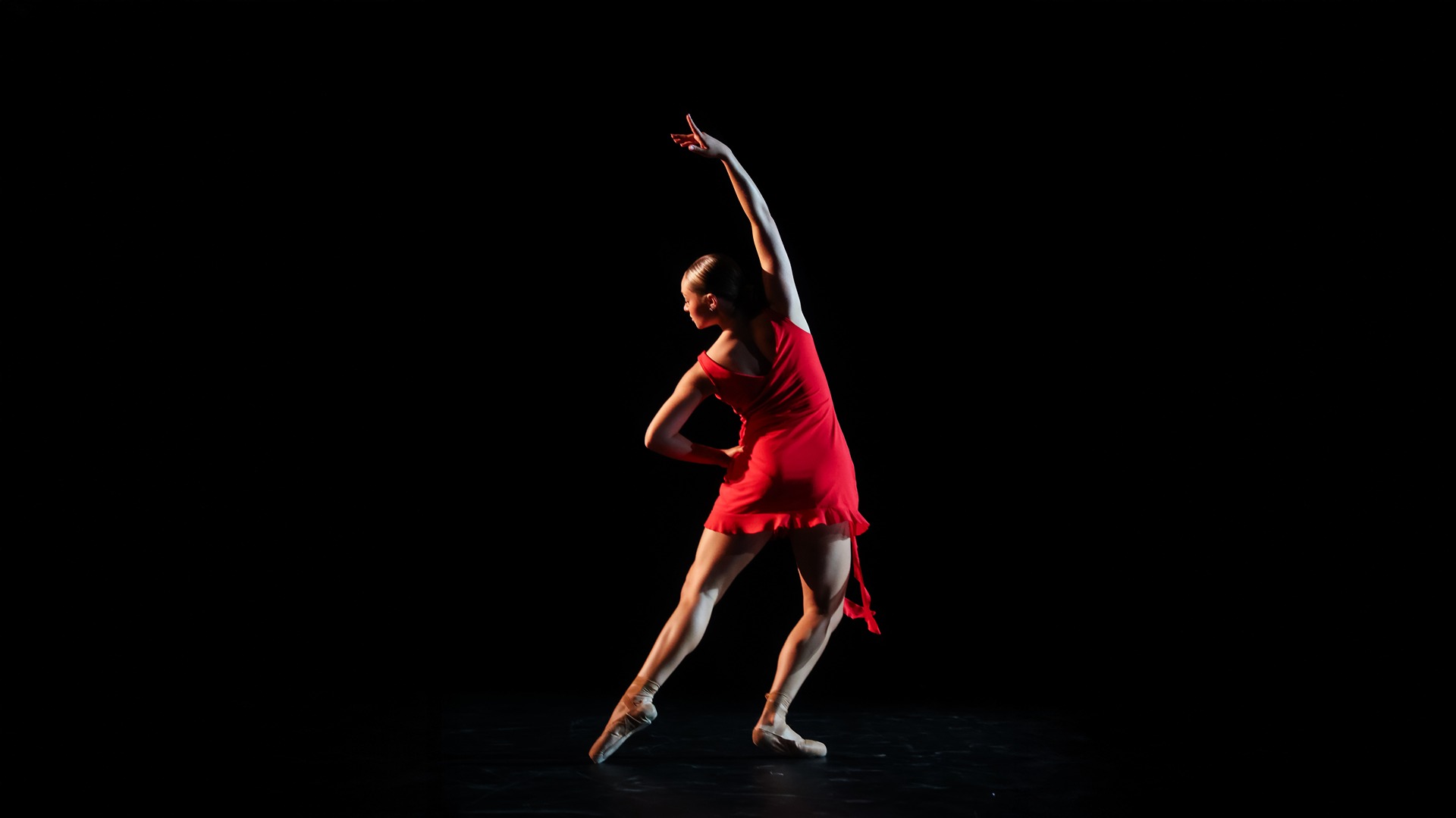A single dancer in a red dress with an all dark surrounding.