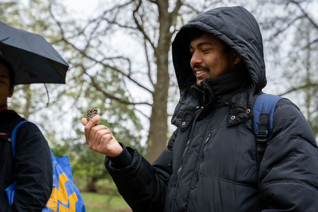 Student wearing rain coat holding pine cone.