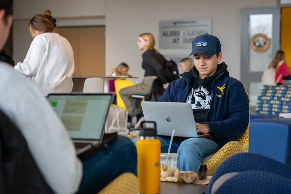 Two students working on laptops in the Reynolds Hall Lobby with snacks and coffee on the table between them.