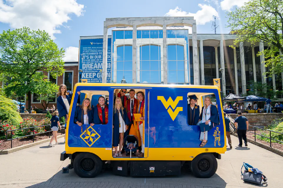 Students pose inside and beside a WVU PRT car in front of the Mountainlair during GradFest.