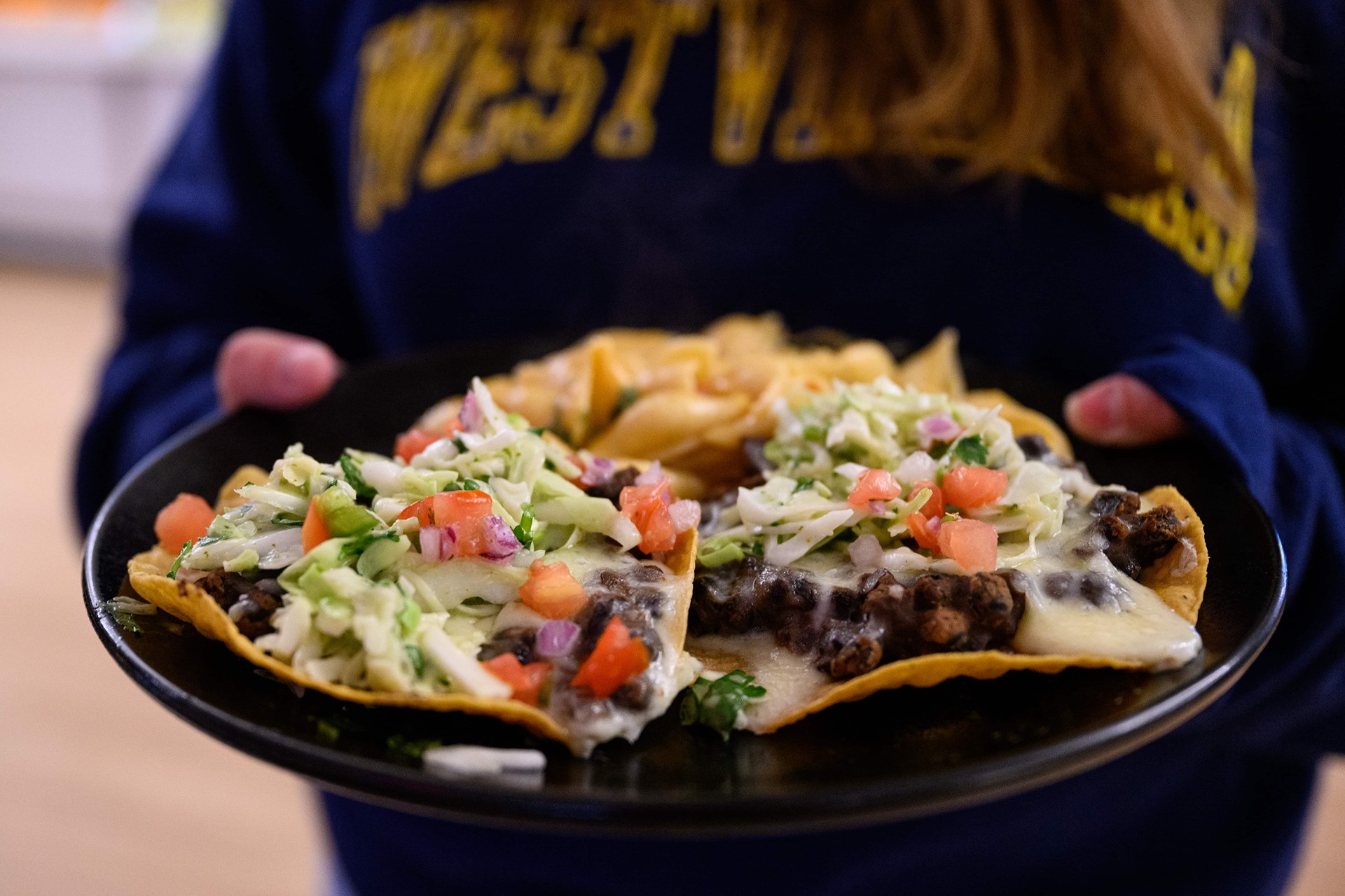 A student wearing a WVU crew neck holding a plate of loaded tacos.