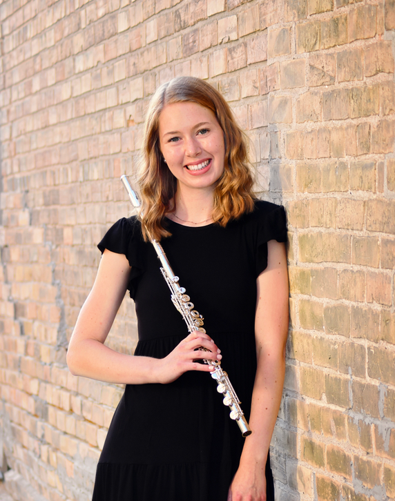 Greta Hulterstrum stands smiling against a light brick wall, wearing a black dress and holding a silver flute.